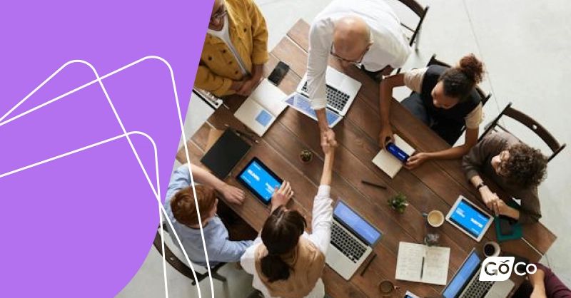 A team shakes hands over a table with laptops to discuss intranet software pricing.