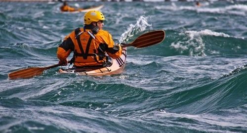 Kayaker using a paddle to navigate choppy coastal waves