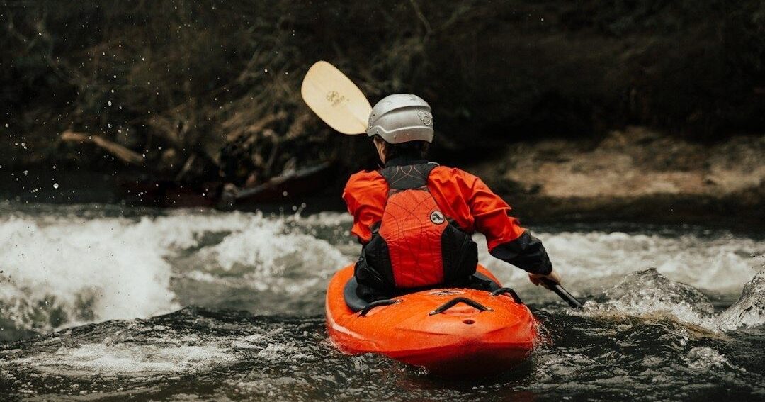 Kayaker in helmet paddling an orange boat through whitewater