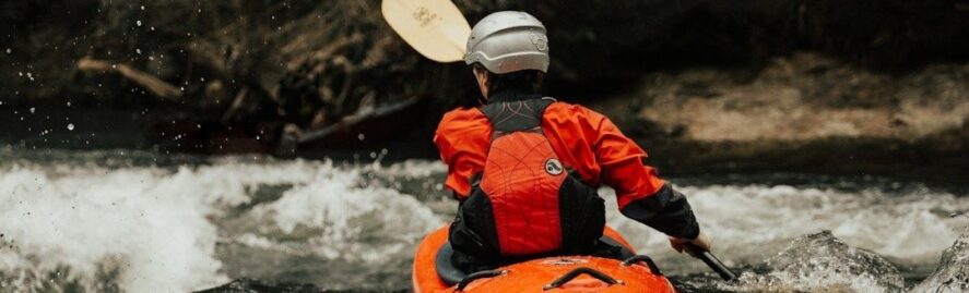 Kayaker in helmet paddling an orange boat through whitewater